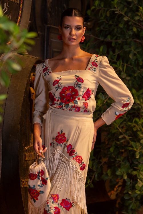 Modelo vistiendo conjunto Fino de Káhyra, bordado de flores y con flecos, falda y top, disponible en color negro, beige y verde.
